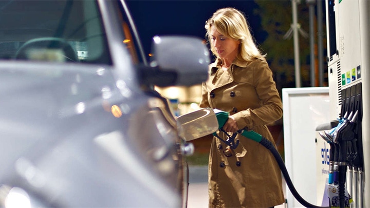 Mujer llenando el depósito del coche en una gasolinera cuya marquesina tiene instalada la intensa iluminación de Philips.