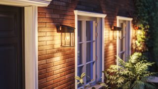 El moderno aplique LED de exterior ilumina el exterior de madera rústica, mostrando soluciones de iluminación de bajo consumo y resistentes a la intemperie para fachadas y porches de casas contemporáneas.