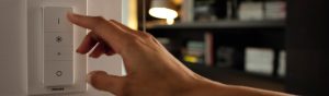 "Mano ajustando el interruptor regulador de luz LED inteligente Philips, controlando la iluminación ambiental en un acogedor salón con estanterías".